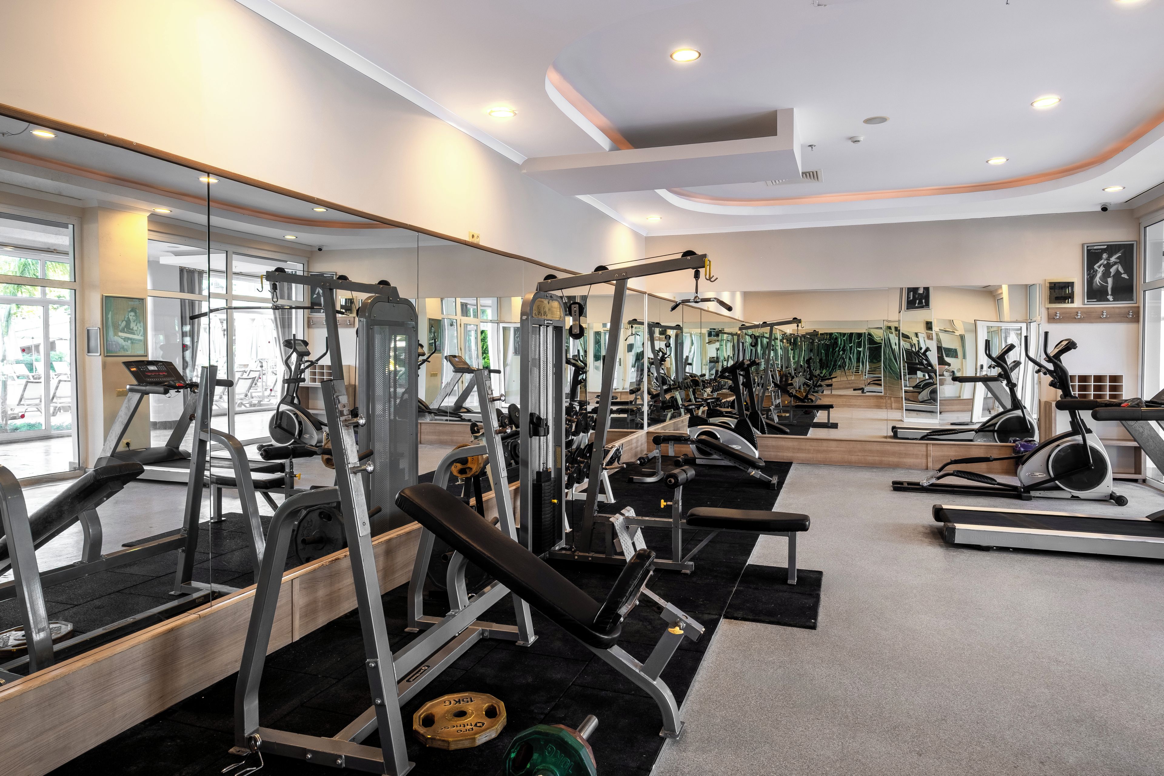 Un gimnasio con equipo de ejercicio variado, ventanas amplias y espejos.