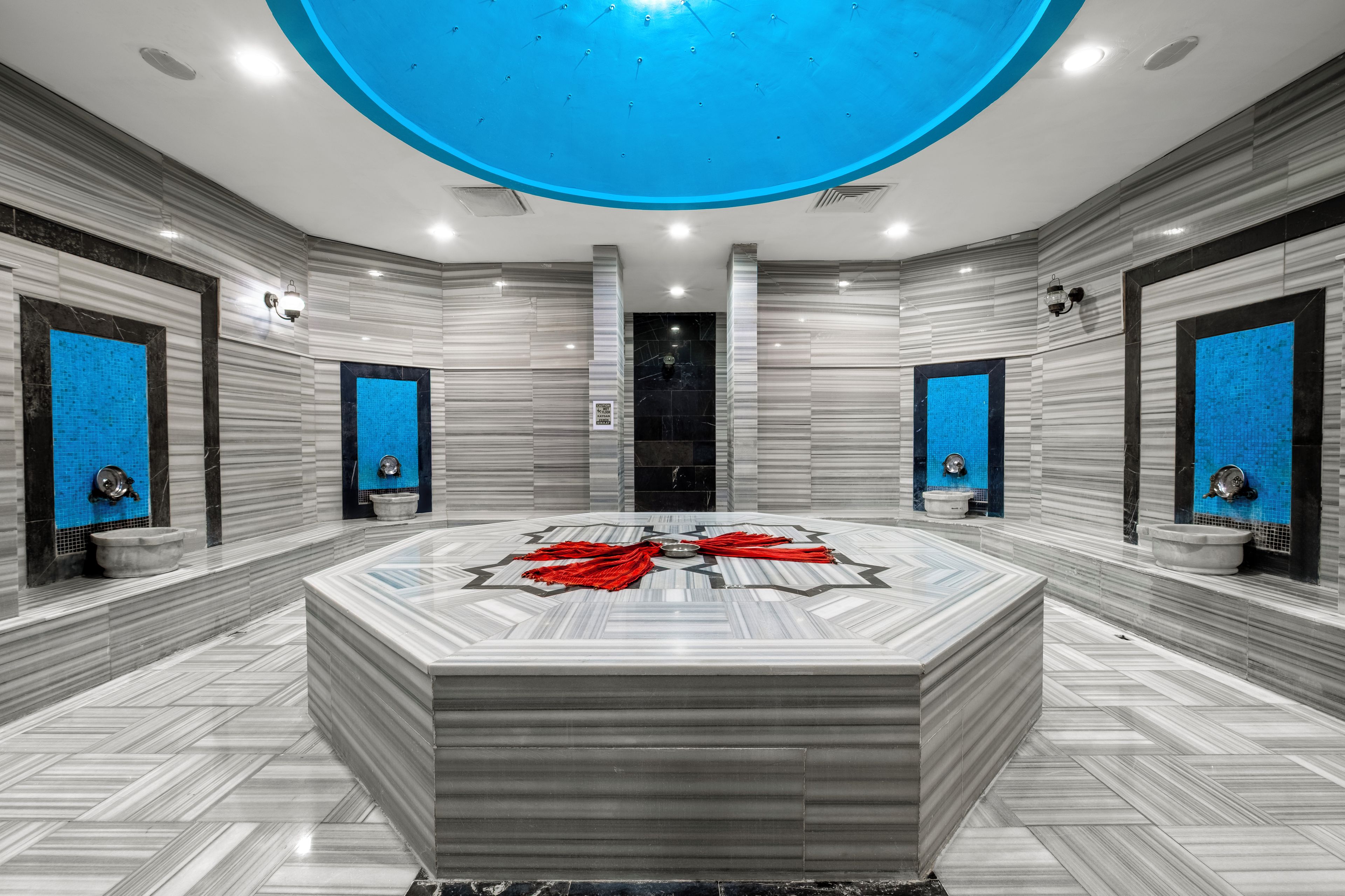 Un baño espacioso con una bañera central grande, dos lavamanos y un techo iluminado con luz azul.
