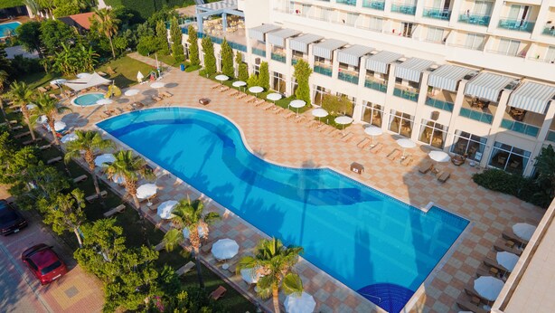 A large swimming pool with sun loungers and umbrellas, surrounded by a building with multiple balconies and a checkered floor pattern. - Solivia Hotel (Konaklı)