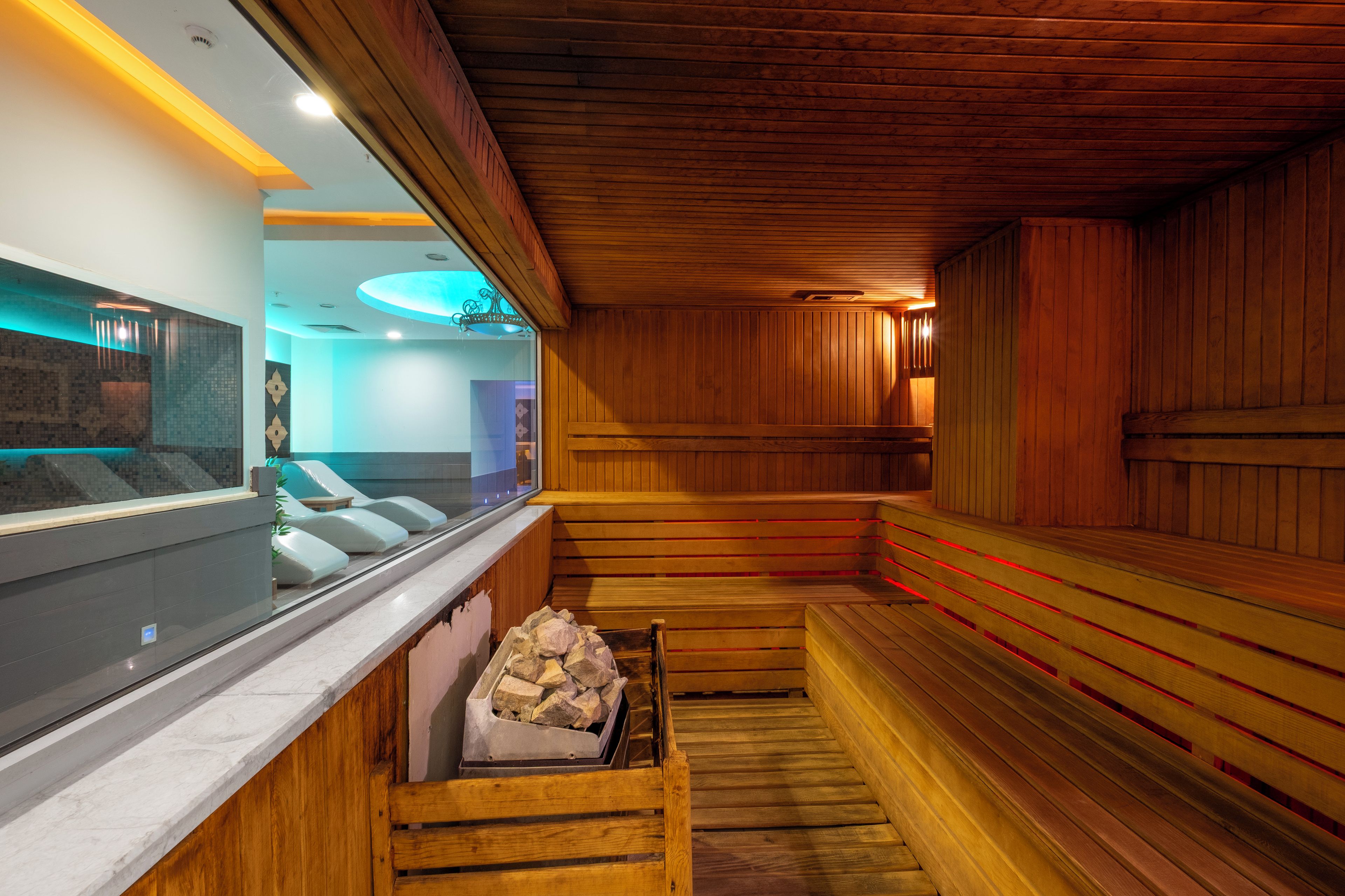 A sauna with wooden benches, a stone bench, and a wall with a window.