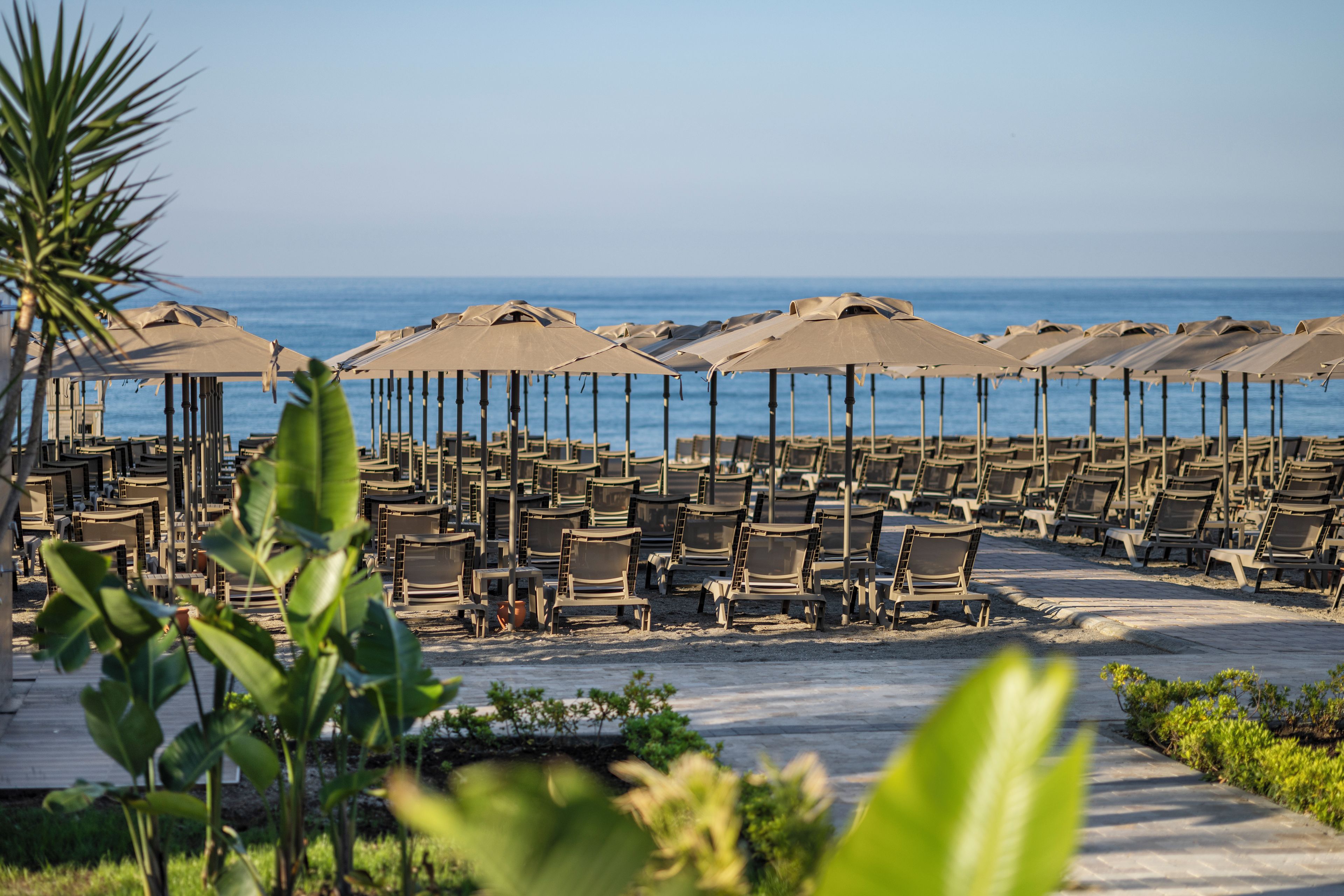 Ein Sitzbereich am Strand mit Stuhlreihen und Sonnenschirmen mit Blick aufs Meer.