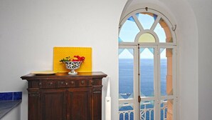 Ein Zimmer mit einem Holzkasten, einer gelb strukturierten Wand und einem Fenster mit Blick aufs Meer.