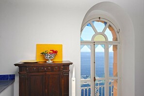 Ein Zimmer mit einem Holzkasten, einer gelb strukturierten Wand und einem Fenster mit Blick aufs Meer.