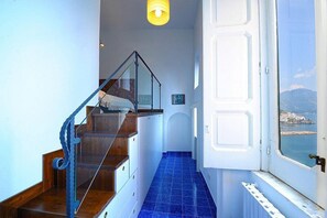 A staircase with a glass railing, a blue-tiled floor, and a view of the sea through an open door. - Villa Elidea B: An elegant and welcoming two-story apartment which faces the sun and the sea, with Free WI-FI. (Amalfi)