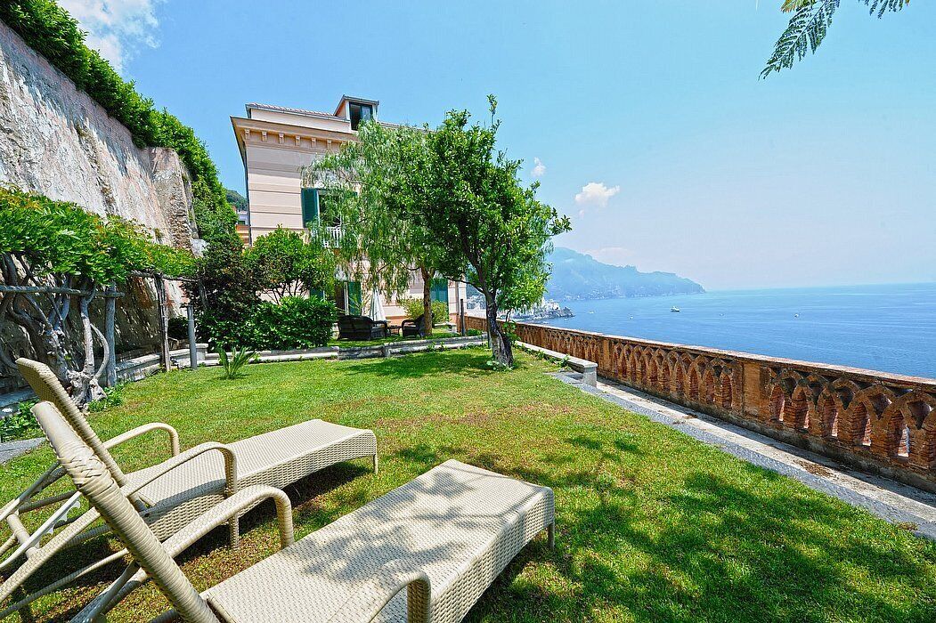 A coastal property with a grassy lawn, wicker lounge chairs, and a view of the sea.