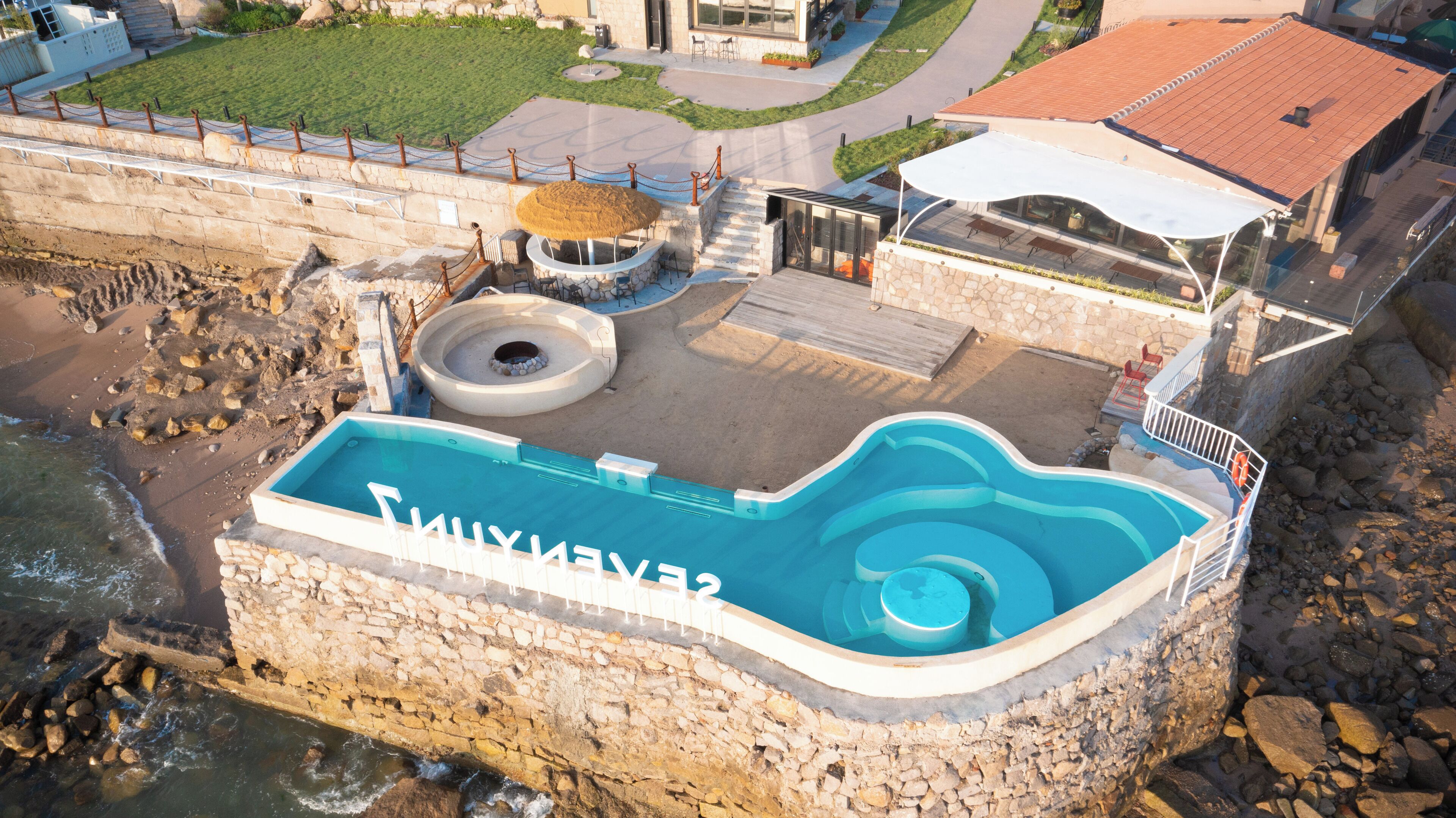 Oversigtsbillede af en swimmingpool med en stenvæg, et loungeområde og udsigt over det omkringliggende landskab.