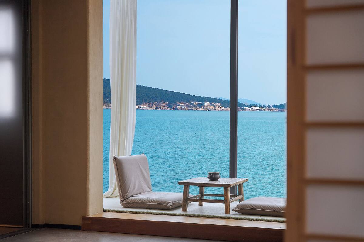 Habitación con un amplio ventanal que da a una masa de agua y a una costa distante.