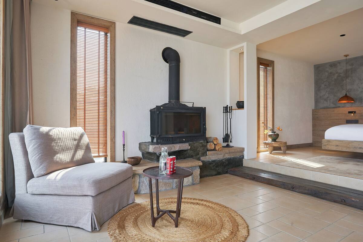 Una sala de estar acogedora con chimenea, un sofá, una mesita y una cama al fondo.