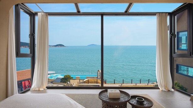 A bedroom with a large sliding glass door leading to a balcony overlooking a sea view. - Nordsee Manor by Arcadia Collection (Qingdao)