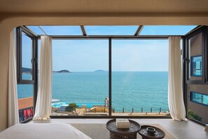 A bedroom with a large sliding glass door leading to a balcony overlooking a sea view. - Nordsee Manor by Arcadia Collection (Qingdao)