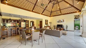 A spacious living area with a high ceiling, a dining table, sofas, and a kitchen area with a large island. - Spacious 4BR - Villa Santai - Central Seminyak (Badung)