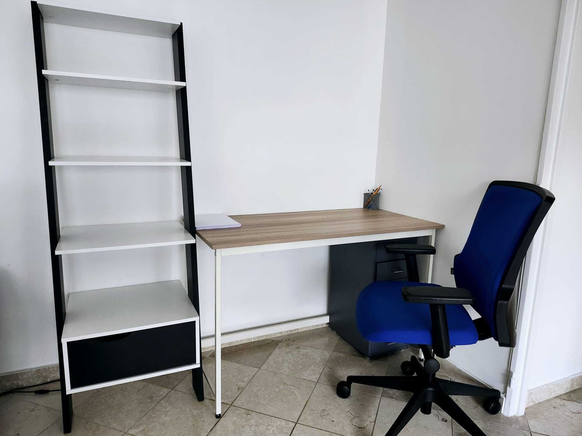A workspace with a white desk, a blue office chair, and a white shelving unit.