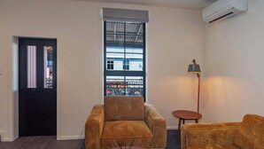 Un salon avec un canapé marron, une table basse ronde ornée d’un objet décoratif, une lampe et une fenêtre donnant sur des immeubles.