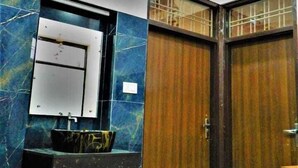 A bathroom with a marble wall, a sink with a mirror, and a wooden door. - Nimbal Elegant Home (Jaipur)
