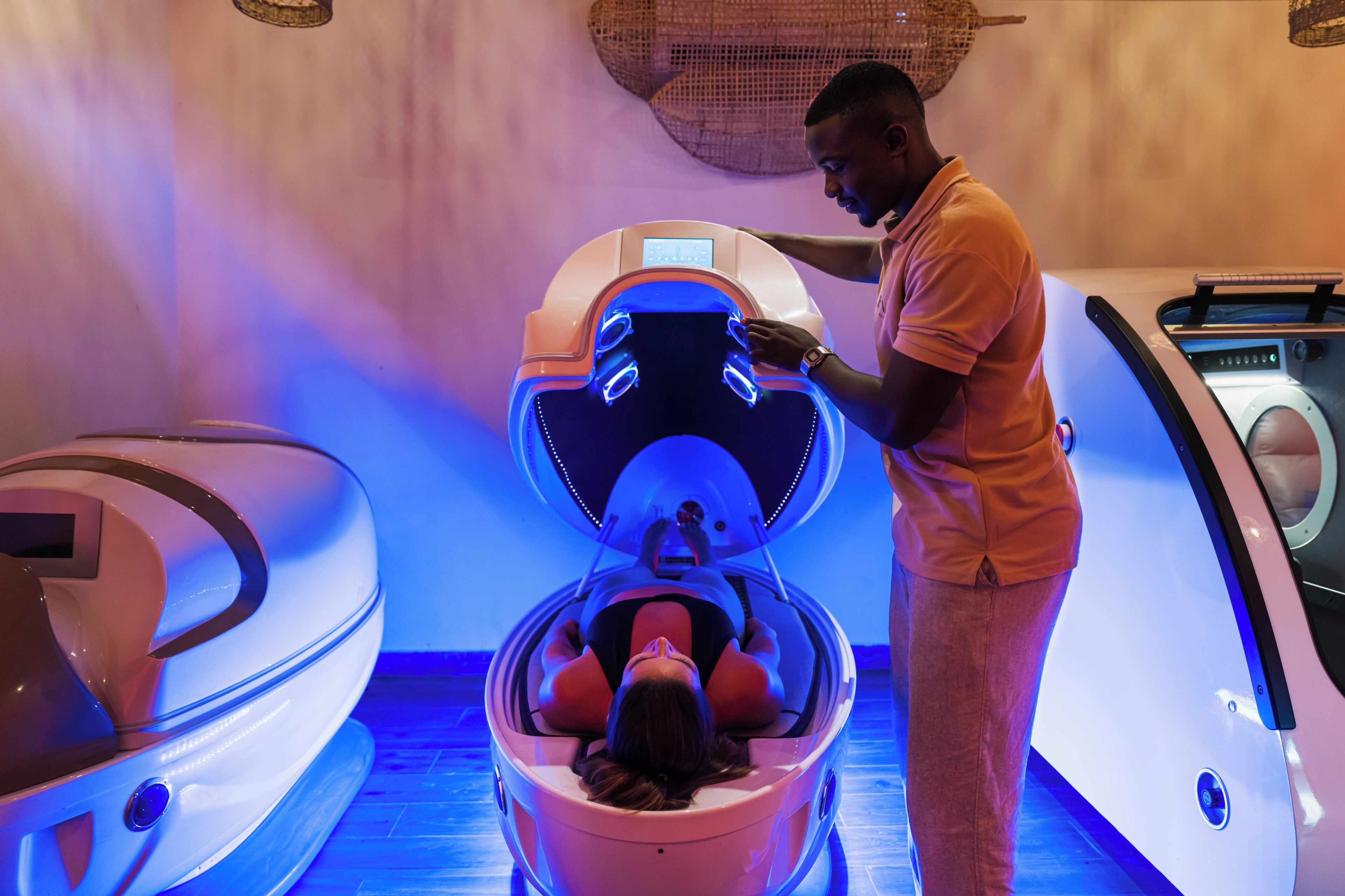 A person operating a massage chair in a room with a blue-lit floor and a large woven basket on the wall.