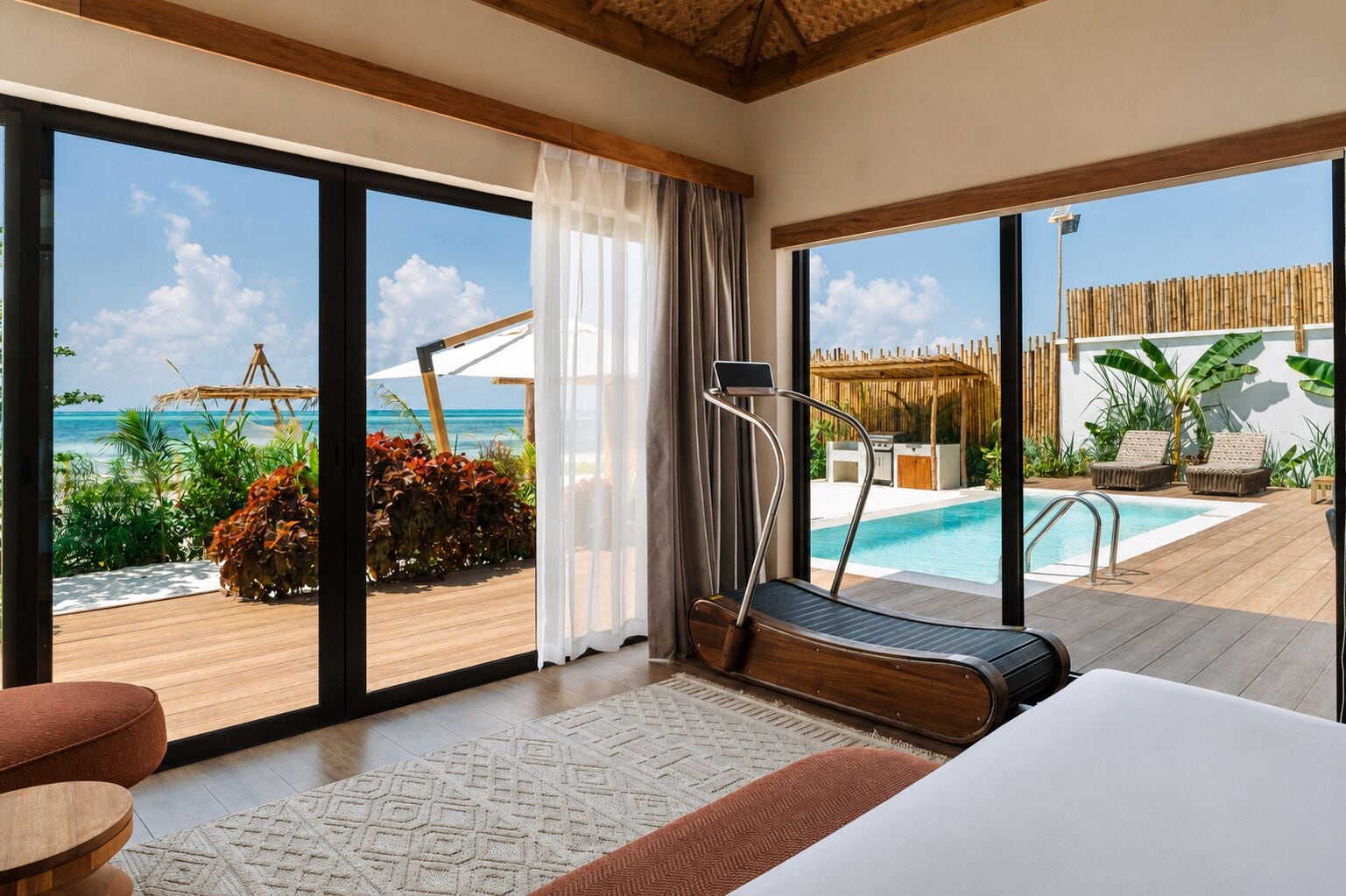 Una habitación con una cinta de correr, una cama y vistas a una piscina y una playa.