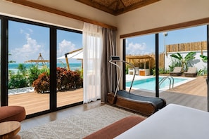 A room with a treadmill, a bed, and a view of a pool and beach.
