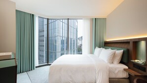 A modern hotel room with a large bed, a desk, and a view of a cityscape through floor-to-ceiling windows. - Oani (Taipei)