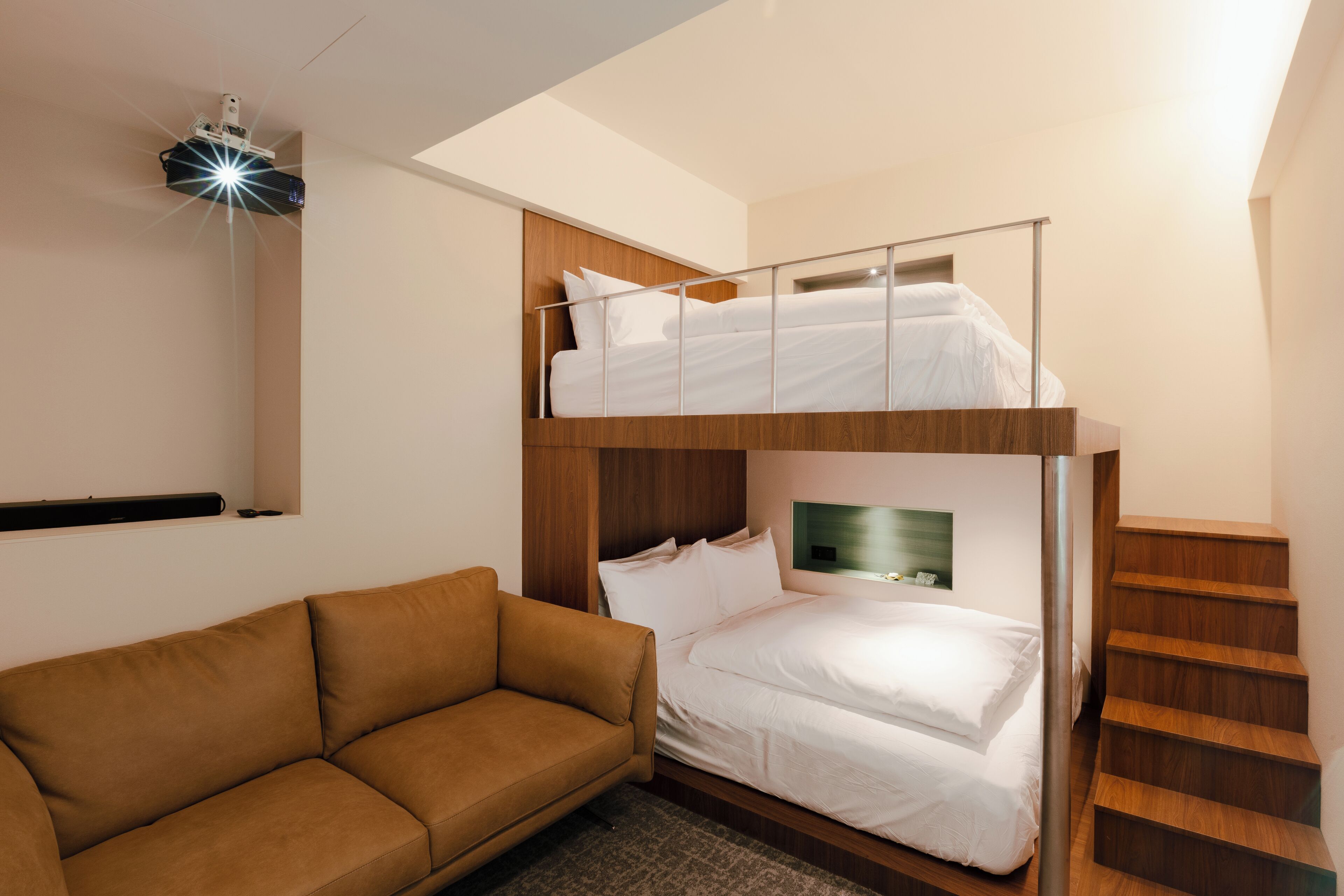 A bunk bed with a wooden headboard, a brown sofa, and a staircase.