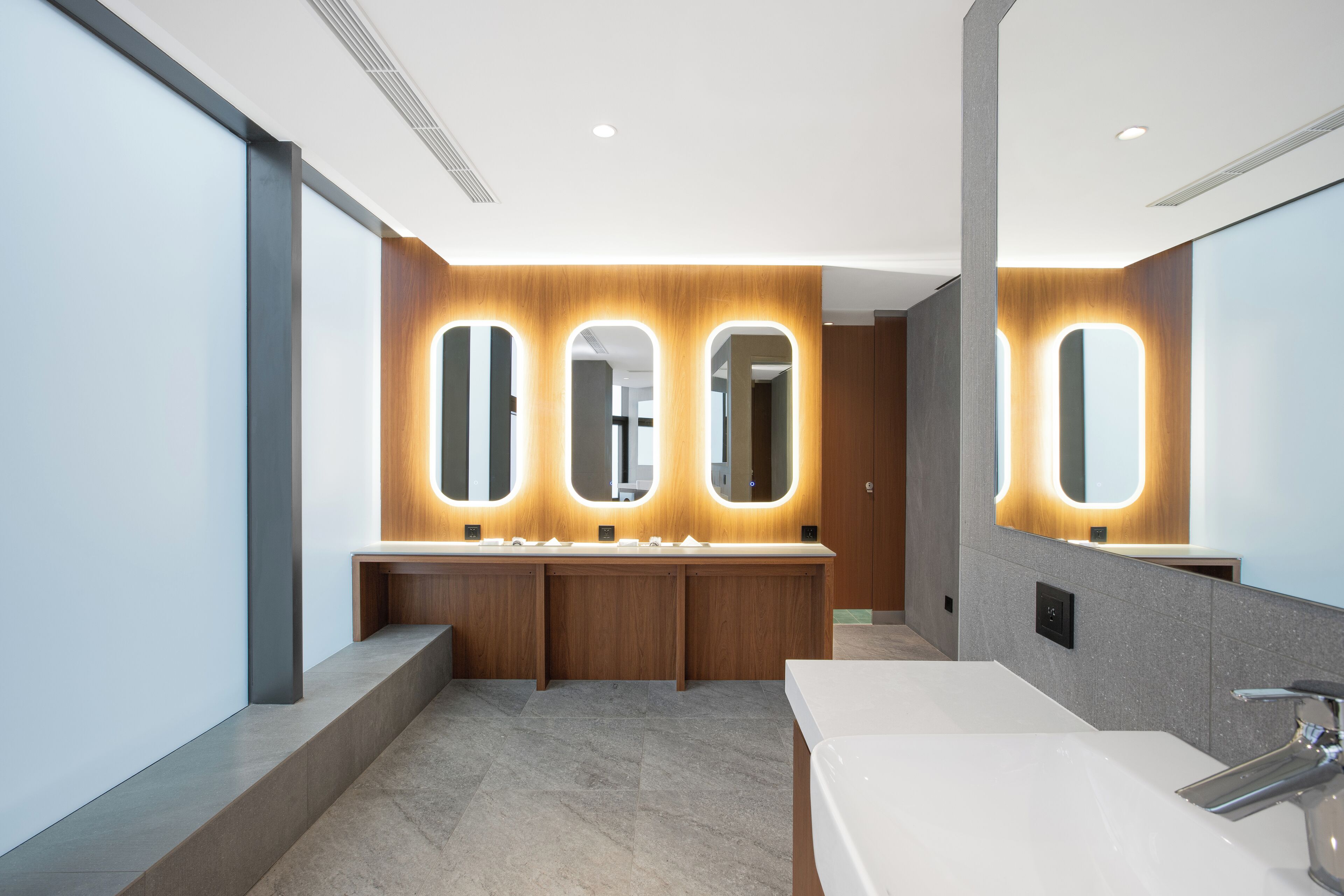 A modern bathroom with a large mirror, three illuminated mirrors above the sink, and a single sink with a chrome faucet.
