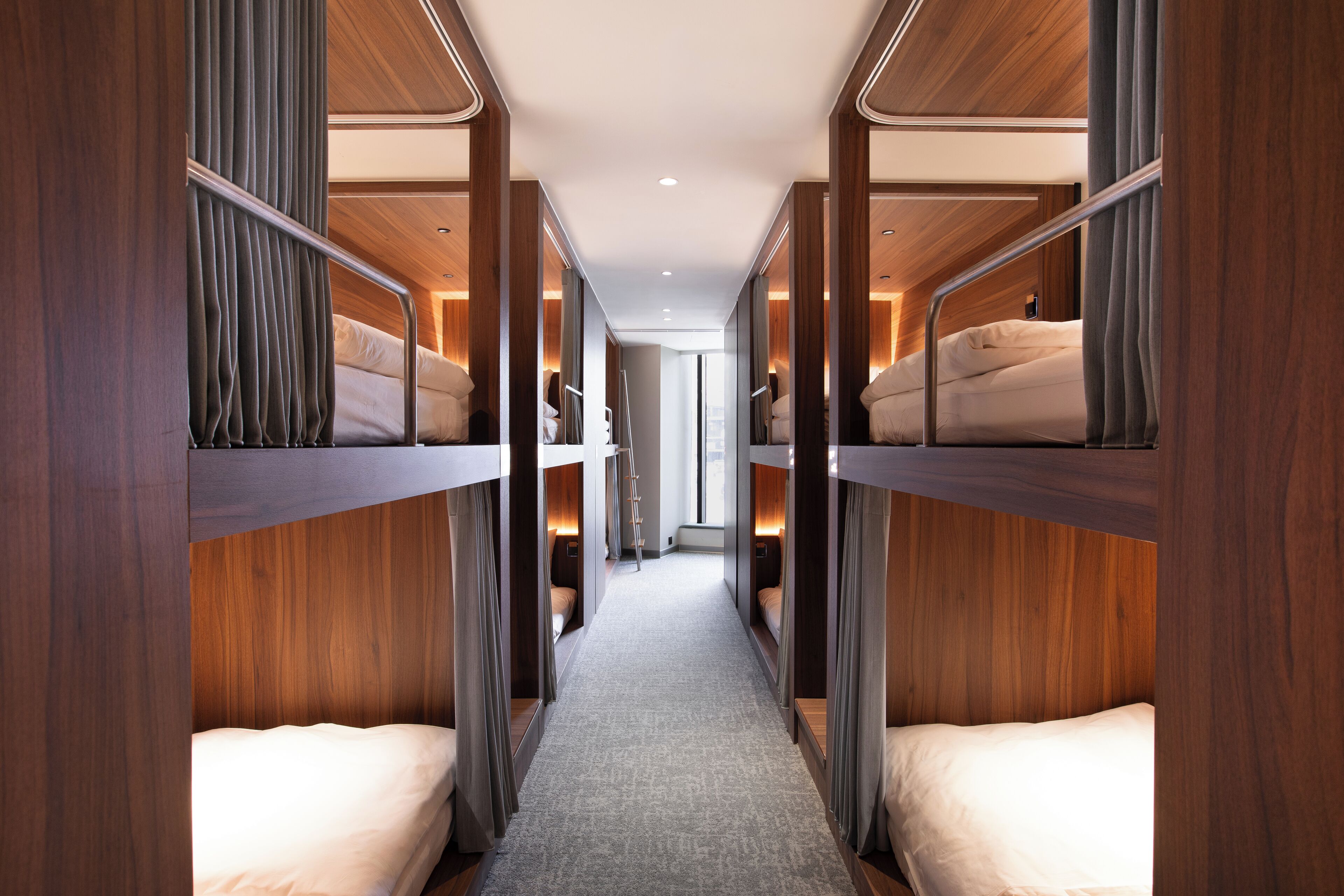 A narrow hallway with bunk beds on either side, wooden paneling, and a carpeted floor.