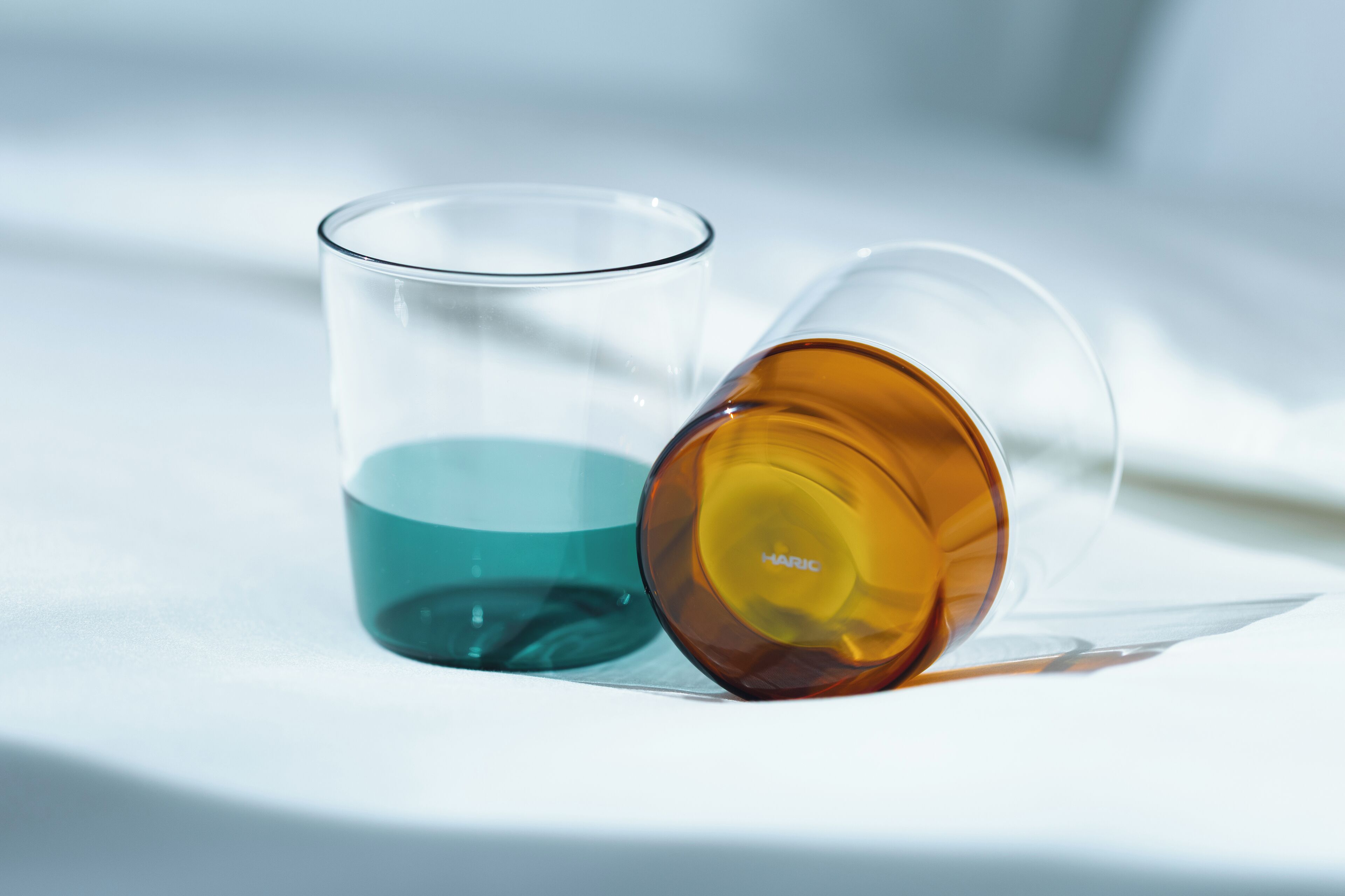 Two clear glasses with different colored liquids, one teal and one amber, on a white surface.