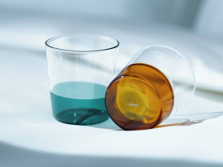 Two clear glasses with different colored liquids, one teal and one amber, on a white surface.