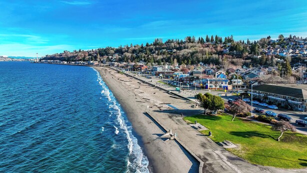Un pueblo costero con playa, casas y un faro a lo lejos.