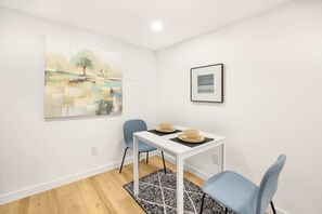 A room with a white table, two blue chairs, a black and white rug, and two paintings on the wall.