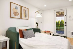 A modern bedroom with a green sofa, white bed, and artwork on the wall.