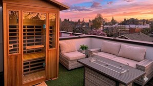 Eine Dachterrasse mit einer Holz-Pergola, zwei Korbsesseln und einem kleinen Tisch.