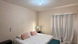 Un dormitorio con cama, mesita de noche, lámpara y cortinas.