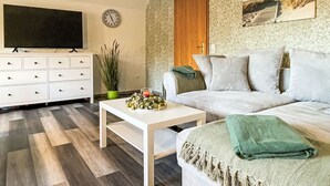 A living room with a sofa, a coffee table, a TV, a clock, and a door. - Die Dorfperle by Interhome (Wanna)