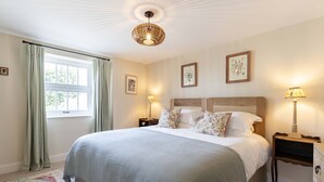 Un dormitorio ordenado con una cama grande, dos mesitas de noche, un ventanal con cortinas y obras de arte en la pared.