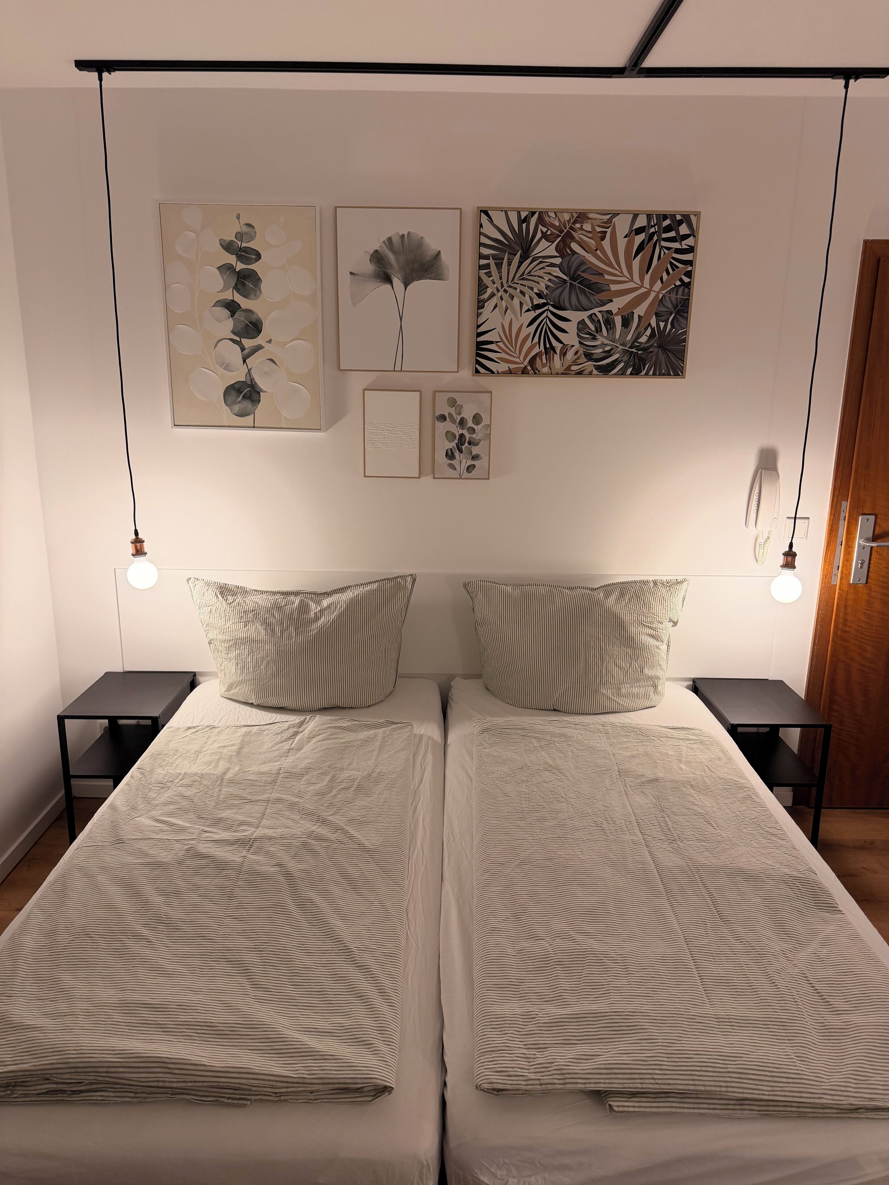 A double bed with striped bedding, two bedside tables, and wall-mounted artwork.
