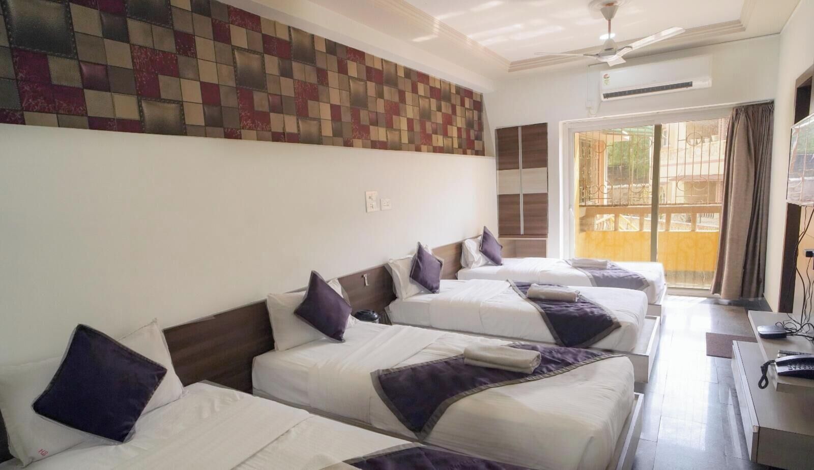 A hotel room with three beds, a ceiling fan, and a view of the outside.