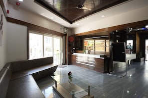 A modern reception area with a glass desk, a bench, and a reception desk with a computer. - Hotel Samrat (Diu)