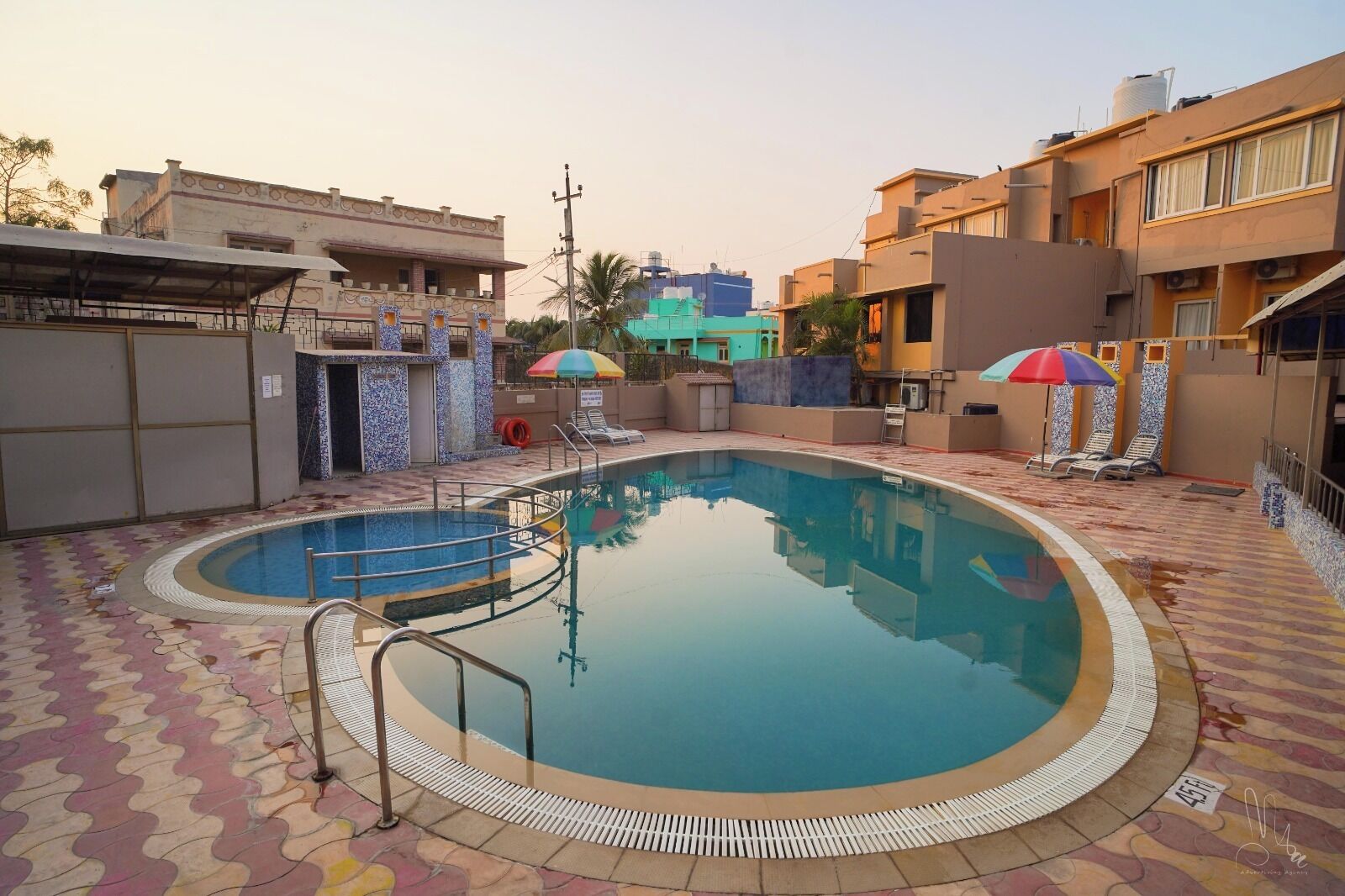 Une piscine avec une terrasse carrelée, un poste de surveillance pour les sauveteurs et des chaises longues équipées de parasols.