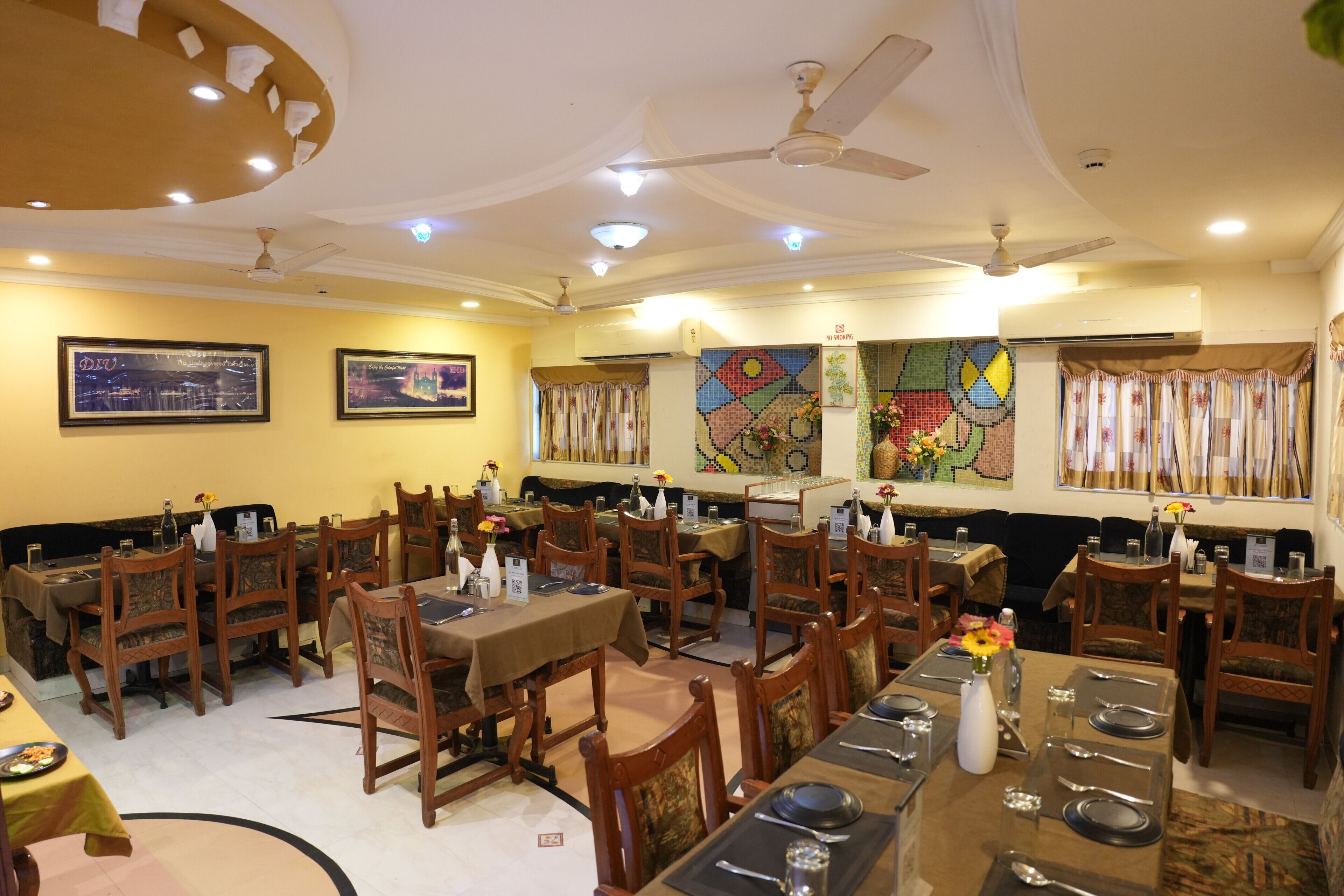 A restaurant with multiple dining tables and chairs, ceiling fans, and wall art.