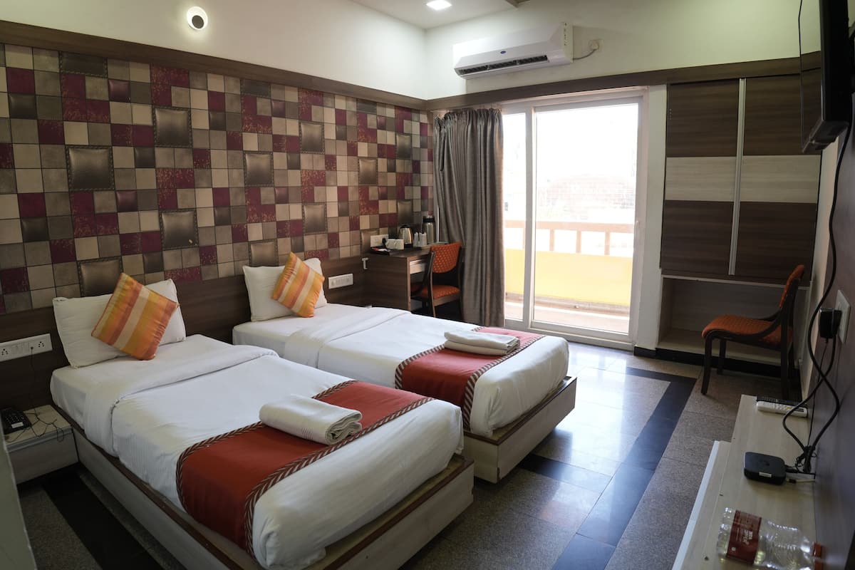 A hotel room with two beds, a desk, a chair, and a view of the outside.
