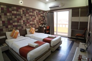 A hotel room with two beds, a desk, a chair, and a view of the outside. - Hotel Samrat (Diu)