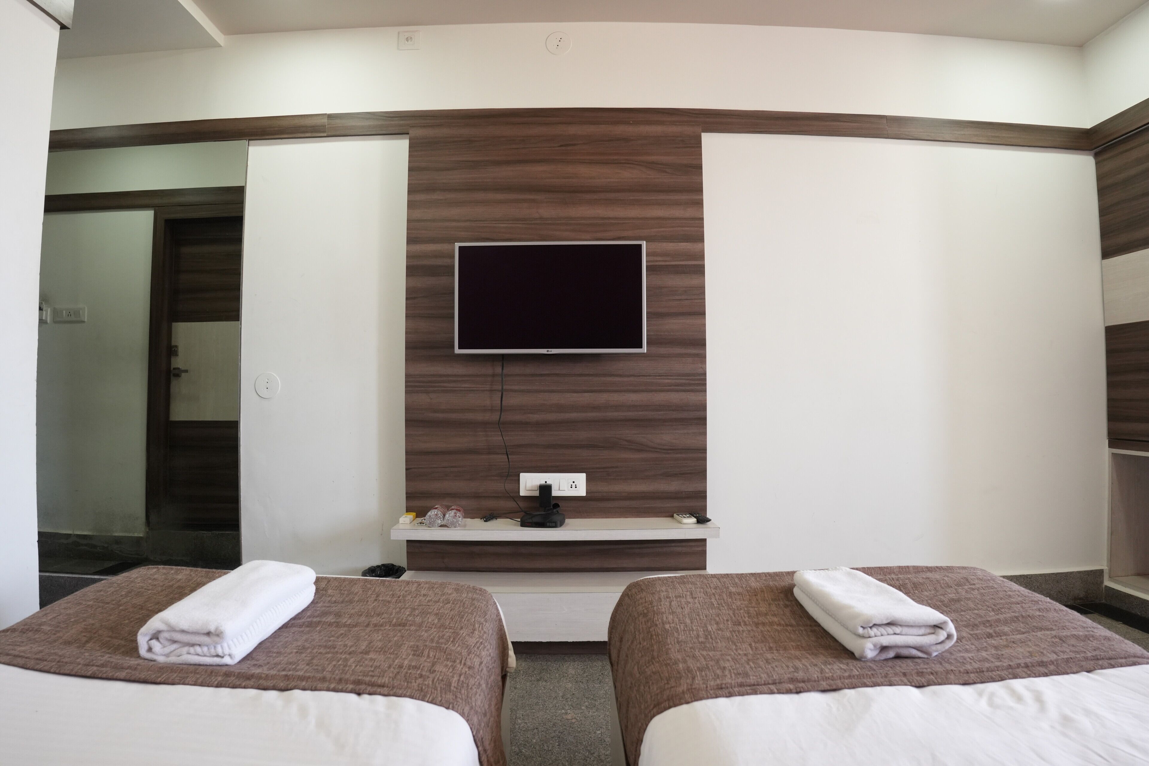 Una habitación de hotel con dos camas, un televisor montado en la pared y un estante con objetos.