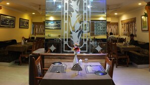 Un restaurante con una mesa central, sillas y un separador decorativo con diseño floral.