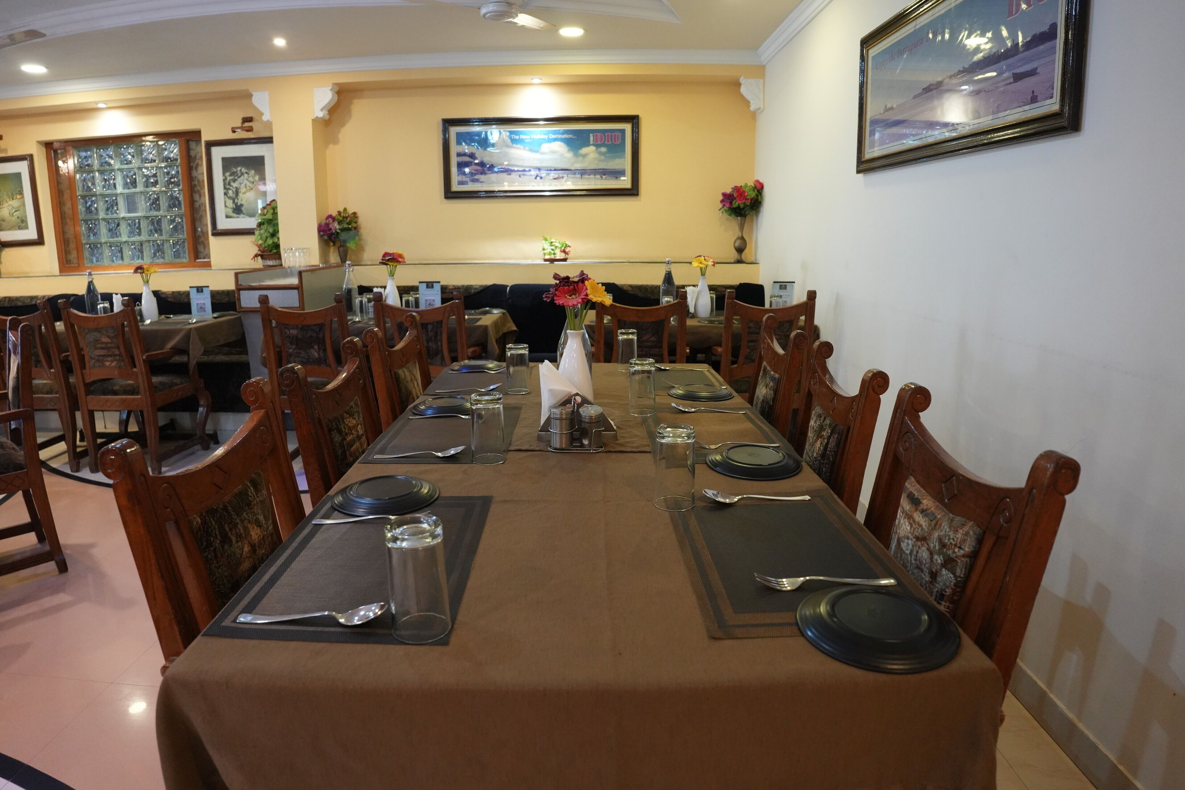 A restaurant with a long table set for dining, wooden chairs, and framed artwork on the walls.