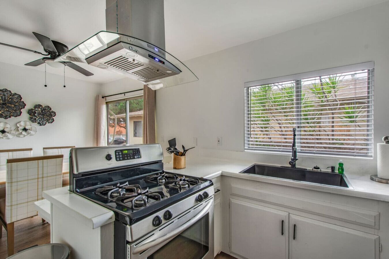 A modern kitchen with a gas stove, a built-in oven, a stainless steel range hood, a window with blinds, and a sink.