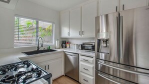 Una cocina moderna con electrodomésticos de acero inoxidable, armarios blancos y una ventana con persianas.