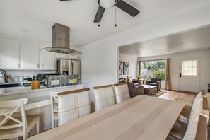 A modern kitchen with white cabinets, a stainless steel refrigerator, and a built-in oven. There is a dining area with a large table and chairs, and a ceiling fan above. - 2Bd/2Bth Close To South Coast Plaza | Restaurants (Santa Ana)