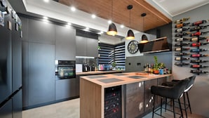 A modern kitchen with a central island, built-in appliances, pendant lighting, and a wine rack on the wall.