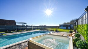 A swimming pool with a hot tub, lounge chairs, and a covered seating area.