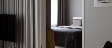 A modern hotel room with a bed, a desk, a chair, a large window, and a view of the outdoors.